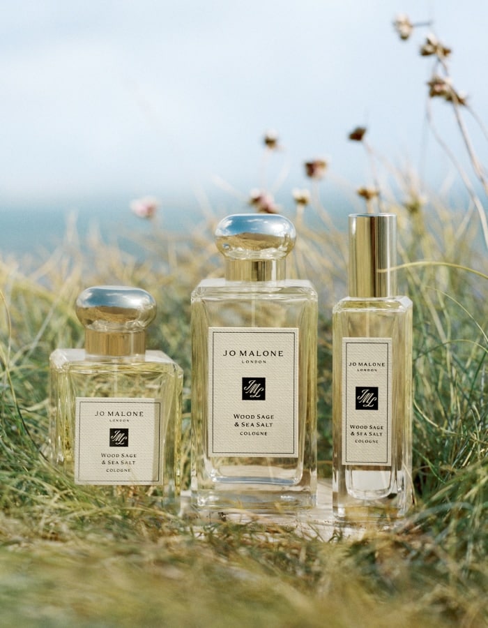 Three Jo Malone London Wood Sage & Sea Salt colognes in varying sizes set in seaside grass.