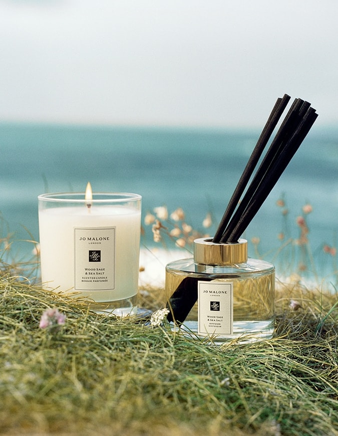 Jo Malone London Wood Sage & Sea Salt scented candle and diffuser set in coastal grass by the ocean.